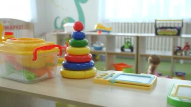 Renkli plastik piramit ve anaokulunun oyun odasındaki ahşap rafta duran farklı oyuncaklar. Küçük çocukların gelişimi