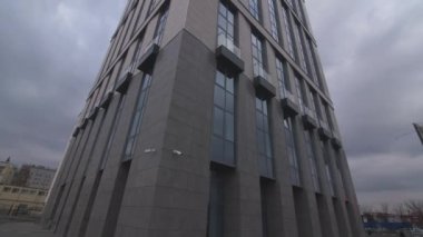 Ofis binasının köşesinde yüksek camlı ve gri taşlı cephe alçak açılı bulutlu bir gökyüzü altında. Şehir mimarisi