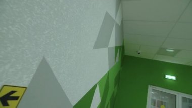 Çağdaş okul binasının uzun boş koridorunda geometrik desenli yeşil duvar.