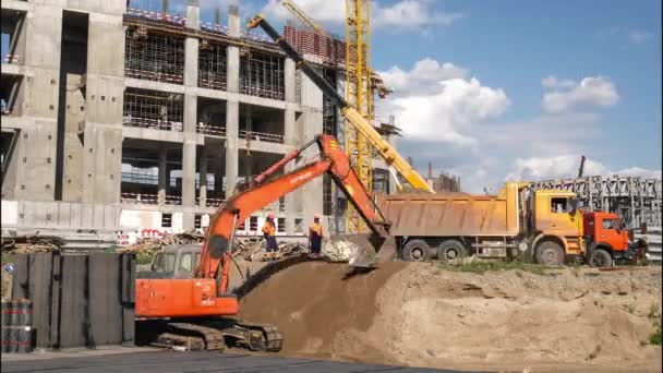 掘削機は 晴れた夏の日のタイムラプスのスポーツスタジアム建設現場で転倒トラックから荷降ろし土を平野 — ストック動画