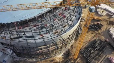 Metal çerçeveli çatı spor arenası ve şehir manzaralı güçlü kule vinci.