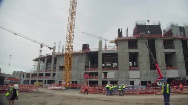 Omsk ロシア 2021年9月15日 黄色のベストウォークの建設業者のグループとオムスクの9月15日に都市建設現場で未完成のスタジアムビルの近くで働く準備 — ストック動画