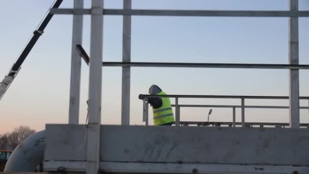 黄背心工人侧卧在工业综合体大型管道系统的月台栏杆上 看晚景 — 图库视频影像