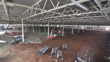 Haftalarca depo binasına zemin kurulumu için zemin işleminin zamanlaması. Metal çerçeveli üretim fabrikası atölyesi. İnşaatçılar ve makineler atölyede