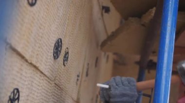 İşçi inşaat alanında yavaş çekiçle ısı yalıtım çarşafını duvara bağlıyor. Bina ısınıyor