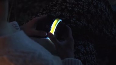 Kadının elinde yarı karanlık bir odada parlayan dijital bir cihaz var. Bayan evde dinlenirken elektronik oyuncak kullanıyor.