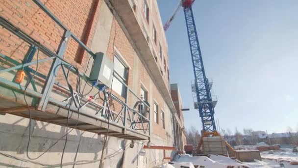 冬の日に再建中の古い工場の建物の近くにゆりかごと高いタワークレーン 工事現場 — ストック動画