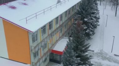 Kış günü bahçesinde karlı çatısı ve köknar ağaçları olan yatılı okul binası. Tahtada çalışma ve dinlenme yeri