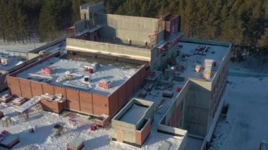 Eski fabrika binasının karlı çatısında güneş batarken çam ormanlarının yakınında kuş bakışı manzaralı malzemeler vardı. Fabrikanın yeniden inşası