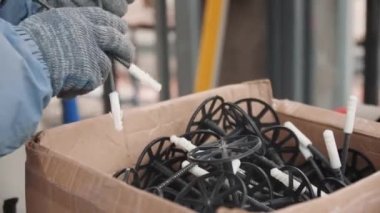 Tekstil eldivenleri giyen işçiler karton kutudan kolları bağlı plastik çiviler alırlar. İnşaat alanı ekipmanları yavaş çekimde kapanır