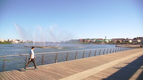 Man Walks Fast Empty Embankment Boardwalk High Fountain Lake Sunny — Stock Video