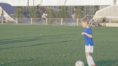 KAZAN, TATARSTAN RUSSIA - 06 Temmuz 2021: Küçük çocuk futbol antrenmanı sırasında topa vuruyor ve yeşil alanda ağır çekimde koşuyor. Kazan 'da 6 Temmuz' da gençler spor takımı katılımcısı