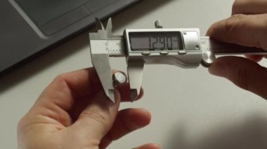 İnsan, iş yerindeki aydınlık oda makro manzarasında, dijital kalibreli cıvata başlığını ölçer. Çağdaş mühendis aracı