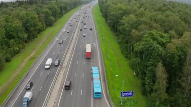 Arabalar, kasvetli gündüz kuşbakışı manzaralı yeşil orman boyunca uzanan modern otoyol boyunca sürüyorlar. Kırsal kesimde otoyol trafiği