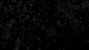 Odaklanamayan ve maviye boyanmış kar taneleri siyah arka planda dönüp parlıyor. 4K 'da kar örtüsü. Alfa kanalı. Siyah arka plana düşen Noel Karı. Rüzgarla hareket eden kar taneleri