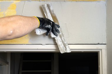 Kapatın. Sıvacı duvara macun bıçağıyla sıva yapıyor.