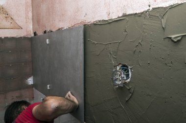 Laying wall ceramic tile. Renovating the wall. Construction worker laying tile over concrete wall using tile levelers, notched trowels and tile glue.