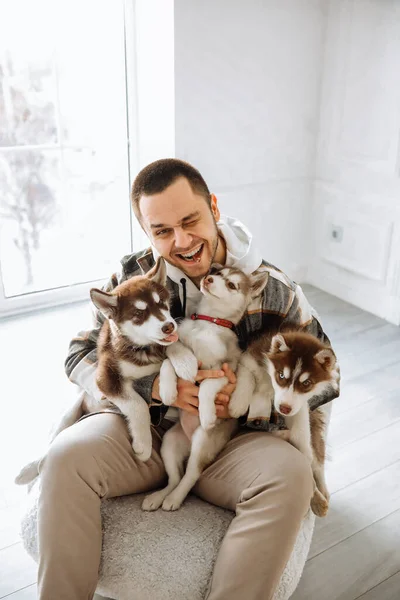 Yavruları beslemek için ağzında sosis tutan bir adam. Avrupalı bir adam kucağında bir sürü köpek yavrusu tutuyor. Yavrularla dolu ev atmosferi.
