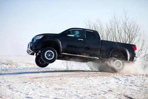 Camion nero che viaggia nella neve e salta — Foto Stock