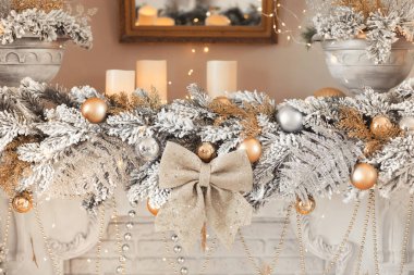 Mumlar, gümüş toplar ve şöminenin üzerinde altın bir fiyonk olan bir Noel çelengi kompozisyonu