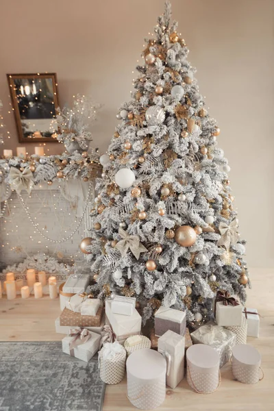 Binnenruimte met een open haard met kaarsen en een versierde kerstboom met cadeautjes. Grote designer sneeuwboom met lampjes en ballen in beige, gouden en zilveren kleuren — Stockfoto