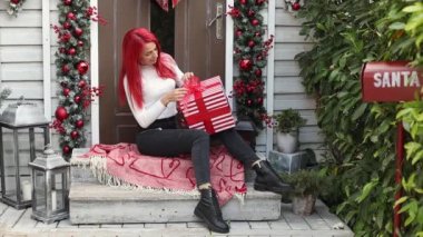 30 yaşında parlak kızıl saçlı, kış tatiline hazırlanan ve evin verandasında çelenk ve çelenkle süslenmiş bir Noel hediyesi paketleyen genç bir kadının portresi. 