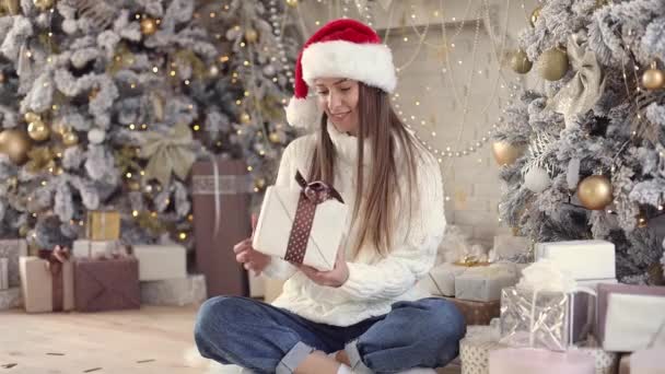 Hermosa mujer joven en suéter blanco acogedor se sienta en casa y abre regalo de vacaciones — Vídeos de Stock