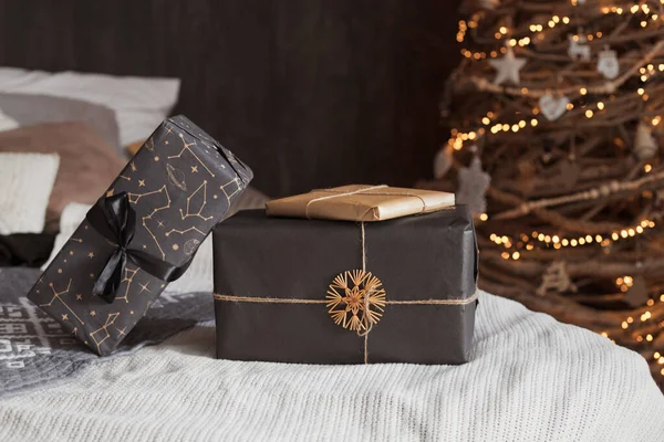Fashion creatief interieur in donkere kleur met een groot tweepersoonsbed versierd met eco-vriendelijke zelfgemaakte houten kerstboom met warme lichten en geschenken verpakt in ambachtelijk papier — Stockfoto