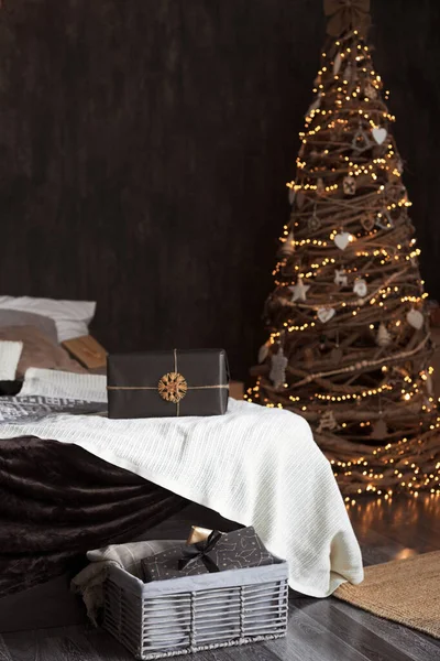 Mode kreativen Interieur in dunkler Farbe mit einem großen Doppelbett mit umweltfreundlichen hausgemachten hölzernen Weihnachtsbaum mit warmen Lichtern und Geschenke in Bastelpapier verpackt dekoriert — Stockfoto