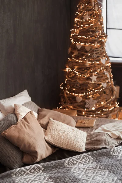 Close-up foto van mode creatief interieur in donkere kleur met een groot aantal kussens op groot tweepersoonsbed versierd eco-vriendelijke zelfgemaakte houten kerstboom met warme lichten — Stockfoto