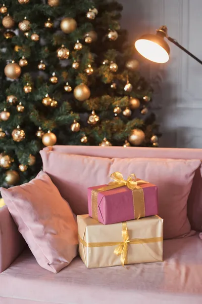 Verticale foto veel geschenkdozen in het interieur van de kamer met een fluwelen bank, zwarte moderne open haard en prachtige versierde kerstboom met in de lounge cadeautjes in goud, licht groen en roze kleur — Stockfoto