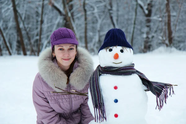 Beautiful girl near a snowman — Stock Photo, Image