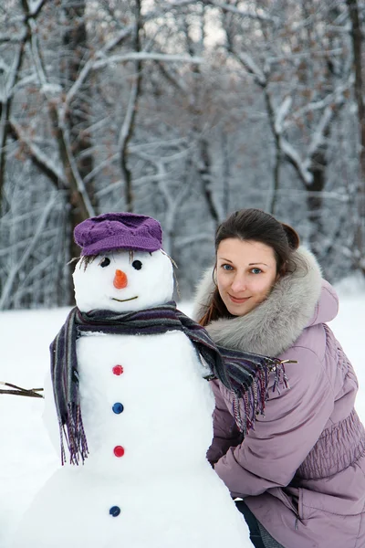 Mooie brunette in de buurt van een sneeuwpop — Stockfoto