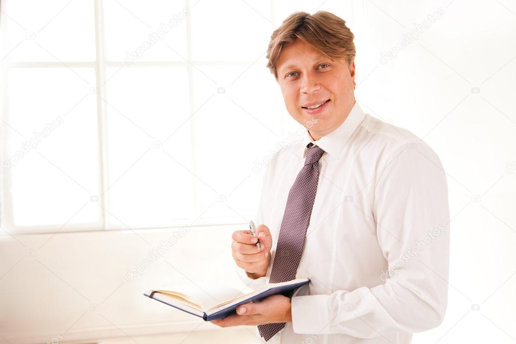 Smiling Businessman in office holding diary