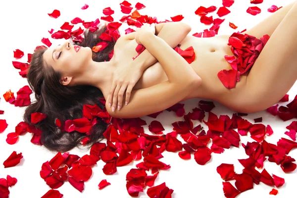 Schlanke Frau liegt auf roten Rosenblättern über weißen — Stockfoto