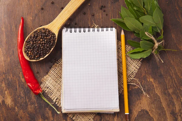 Especias en cucharas, cuaderno sobre fondo de madera — Foto de Stock