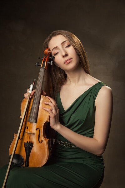 Beautiful young woman playing violin over black