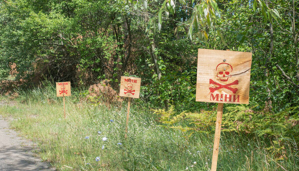 Деревянные знаки в лесу возле дороги, предупреждающие, что территория заминирована. Концепция войны. Текстовая трансляция: шахты