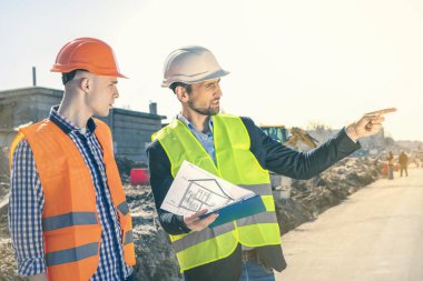 İnşaat mühendisi gurubu bir bina sahasında. İnşaat mühendisiyle Emlak Projesi. İşletme Mühendisleri planları arıyor..