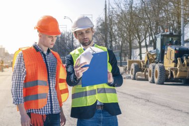 İnşaat mühendisiyle Emlak Projesi. Arazi inşaatı çalışmalarının grafiksel temsili. Arkaplanda Kazıcı ve İnşaat Ekipmanı.