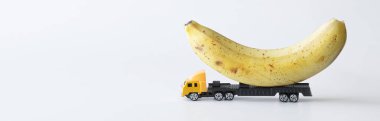 Oyuncak kamyon taze sarı bir muz taşıyor. Beyaz arka plan. Büyük boy eşyalar ve yeni hasattan taze tropikal meyveler için teslimat konsepti. Web afişi. Yakın plan.