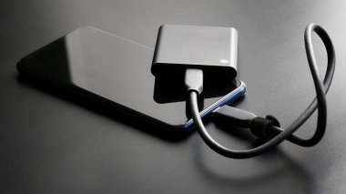Koyu renk gradyan arka planda bir akıllı telefona bağlı harici taşınabilir SSD. Taşınabilir Solid State Drive. OTG arayüzü. Modern teknolojiler, cihazlar ve SSD disk kullanımı kavramı. Yakın plan.