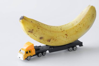 Oyuncak bir kamyon yeni bir ürün taşıyor. Taze sarı bir muz. Beyaz arka plan. Büyük boy eşyalar ve taze tropikal meyveler için teslimat konsepti. Yakın plan.