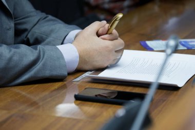 Takım elbiseli bir adam hoparlörün önündeki masada oturuyor. Toplantı, seminer ya da profesyonellerin pazarlığı. Girişimci, avukat, sigortacı, şerif yardımcısı ya da resmi. Yüzü yok