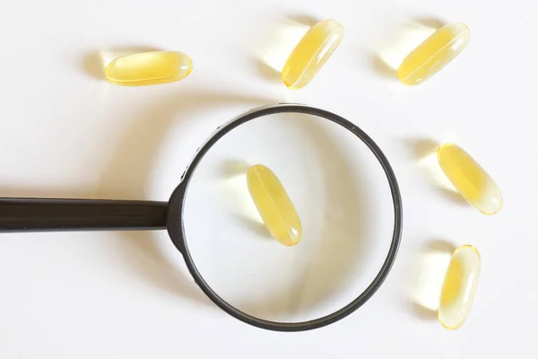 Cápsulas Gel Con Medicamento Amarillo Una Lupa Sobre Fondo Blanco — Foto de Stock