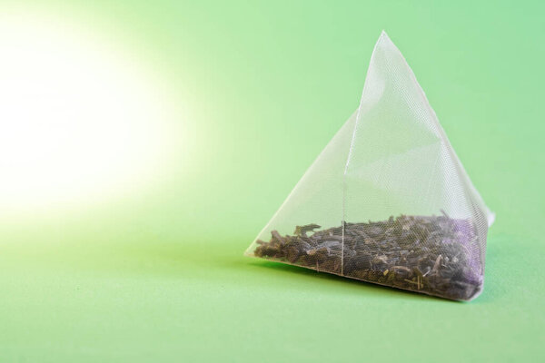 Пирамида пакетика чая с зеленым чаем на зеленом фоне. Выпивка для долгожителя. Макро. Мелкая глубина резкости