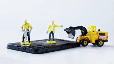 Oyuncak adam işçileri eski bir cep telefonunu ya da akıllı telefonu matkap ve forklift kamyonuyla onarıyor ya da elden çıkartıyorlar. Akıllı telefon tamiri ya da geri dönüşüm konsepti. Mikro dünya. Yakın plan.