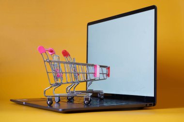 İnce dizüstü bilgisayar ya da ultrabook ve sarı arka planda süpermarketten iki araba. Sitelerden alışveriş ve modern online ticaret kavramı. Bir yazı için boş yer. Gün ışığı