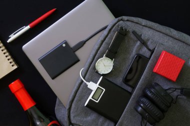 Şehir seyahati için küçük bir sırt çantası ya da laptop, elektrik bankası ve SSD, kablosuz kulaklık ve akıllı telefon, kol saati, şişe içinde içki, kalem ve kırmızı hediye kutusu. Aletlerle yaşam tarzı. Yakın plan.
