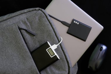 Laptop ya da ultraviyole çantalı küçük tekstil şehri sırt çantası, harici bir SSD, batarya güç bankası ve kablosuz fare. Aletlerle seyahat ve yaşam tarzı. Siyah arka plan. Yakın plan.